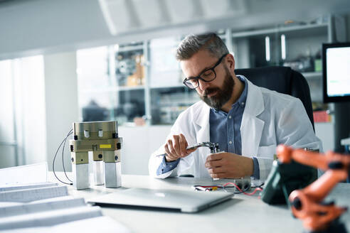 A robotics engineer working on desing of modern robotic arm adn sitting at dest in laboratory. - HPIF00927