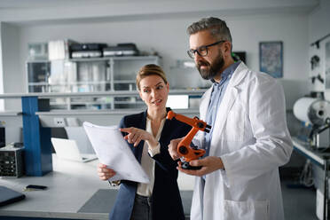 Robotics engineers with blueprints dicussing and desinging a modern robotic arm in laboratory. - HPIF00935