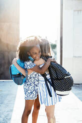 Laughing African American girl embracing friend standing on street in bright day - ADSF40435