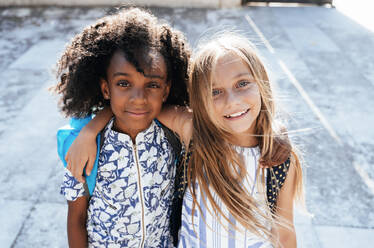 Laughing African American girl embracing friend standing on street in bright day - ADSF40436