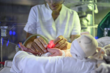 Von oben Ernte Frau Krankenschwester hält kleinen Fuß der kranken winzigen Baby in Säuglingsbrutkasten in ICU im Krankenhaus liegen - ADSF40441