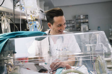 Doctor male attentively taking care of faceless newborn baby lying in incubator in clinic - ADSF40459