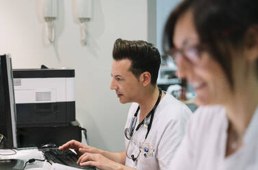 Seitenansicht Arzt mit anonymen Krankenschwester in weißer Uniform arbeiten am Computer im Krankenhaus - ADSF40461
