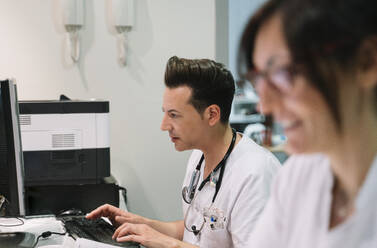 Side view doctor with anonymous nurse in white uniform working at computer in hospital - ADSF40461