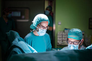 Male doctor and female assistant preparing clean tools before surgery in brightly illuminated operating theater - ADSF40514