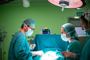 Side view of doctor and assistants in medical uniform performing surgery through cut on patient in modern hospital - ADSF40519