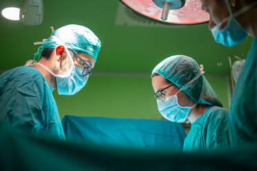 Side view of doctor and assistants in medical uniform performing surgery through cut on patient in modern hospital - ADSF40520