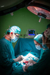 Side view of doctor and assistants in medical uniform performing surgery through cut on patient in modern hospital - ADSF40521