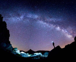 Low angle of tourist with headlamp standing on cliff and admiring amazing starry sky at night in Pyrenees - ADSF40528