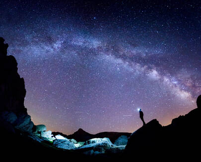 Niedriger Blickwinkel eines Touristen mit Stirnlampe, der auf einer Klippe steht und den atemberaubenden Sternenhimmel bei Nacht in den Pyrenäen bewundert - ADSF40528