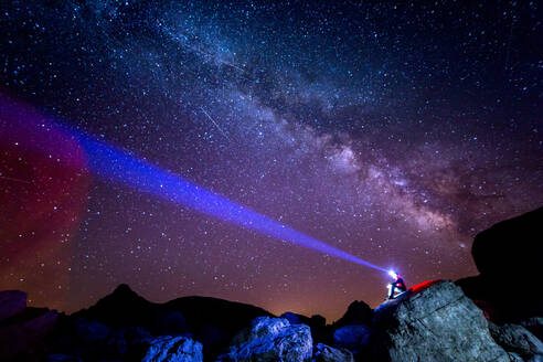 Niedriger Winkel des Touristen mit Stirnlampe sitzt auf einer Klippe und bewundert erstaunliche Sternenhimmel in der Nacht in den Pyrenäen - ADSF40529
