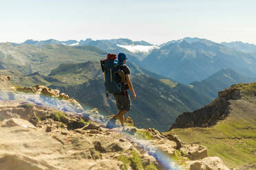 Unbekannter Mann mit Rucksack, der an einem sonnigen Tag in den Pyrenäen spazieren geht und eine Bergkette bewundert - ADSF40533