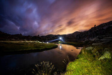 Picturesque scenery of calm river with green grassy shores flowing through mountainous valley with bright light reflected in water surface under colorful cloudy sunset sky in summer evening in Pyrenees - ADSF40541