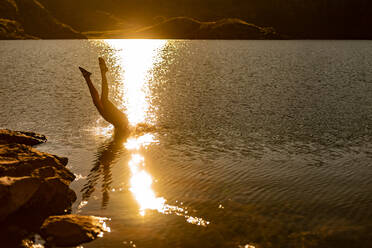 Unerkennbare weibliche Reisende, die in das plätschernde Wasser eines Bergsees springt, in dem sich das Sonnenlicht spiegelt, Sommerabend - ADSF40547