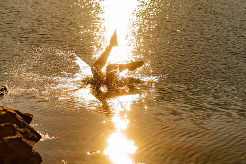 Unerkennbare weibliche Reisende, die in das plätschernde Wasser eines Bergsees springt, in dem sich das Sonnenlicht spiegelt, Sommerabend - ADSF40548