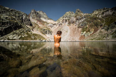 Rückenansicht von unerkennbar anmutigen weiblichen Reisenden stehen in ruhigen kristallklaren See Wasser gegen majestätische felsige Landschaft in den Pyrenäen Berge - ADSF40561