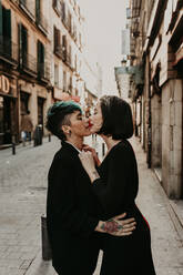 Side view of lesbian couple with piercing and tattoos kissing on street - ADSF40565