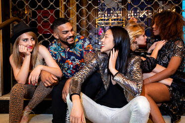 Trendy multirassischen jungen Freunden lächelnd zusammen, während auf konkrete Schritte in der Nacht Partei sitzen - ADSF40743