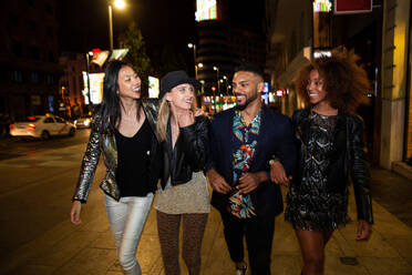 Group of stylish multiracial friends walking together on city street for party at night - ADSF40748