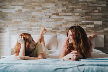 Junge, fröhliche Freunde in Pyjamas, die sich gegenseitig anschauen und auf dem Bett interagieren - ADSF40757