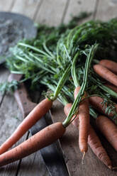 Heap of bright fresh carrots with green stems lying on wooden board on table - ADSF40789