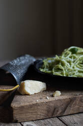 Tasty spaghetti with pesto sauce, spinach and parmesan cheese. Grater and a couple of red wine glasses are shown in the image - ADSF40849