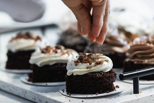 Unbekannter Erntekoch bestreut appetitlichen veganen Biskuitkuchen mit Schokolade, während er in der Küche einer Bäckerei kocht - ADSF40859