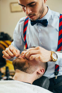 Ein Barbier schneidet den Bart eines Mannes mit einem Rasiermesser in einem Barbershop - ADSF40877