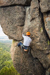 Männlicher Bergsteiger, der mit Sicherheitskarabiner und Seilen einen hohen Felsen erklimmt - ADSF40888