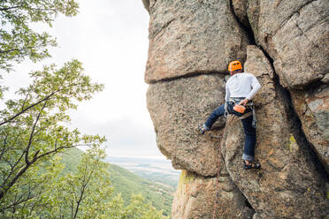 Männlicher Bergsteiger, der mit Sicherheitskarabiner und Seilen einen hohen Felsen erklimmt - ADSF40889