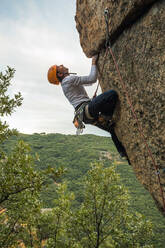 Männlicher Bergsteiger, der mit Sicherheitskarabiner und Seilen einen hohen Felsen erklimmt - ADSF40893