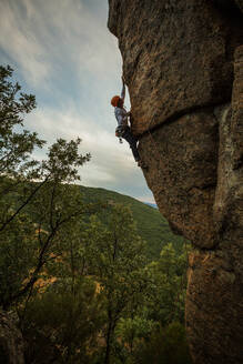 Männlicher Bergsteiger, der mit Sicherheitskarabiner und Seilen einen hohen Felsen erklimmt - ADSF40894