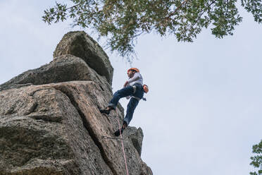 Seitenansicht eines sportlichen männlichen Bergsteigers, der an einem bewölkten Tag auf einem Felsen im Gebirge aufsteigt - ADSF40896