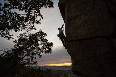 Männlicher Bergsteiger, der mit Sicherheitskarabiner und Seilen einen hohen Felsen erklimmt - ADSF40897