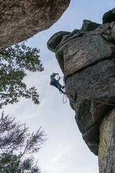 Seitenansicht eines sportlichen männlichen Bergsteigers, der an einem bewölkten Tag auf einem Felsen im Gebirge aufsteigt - ADSF40898