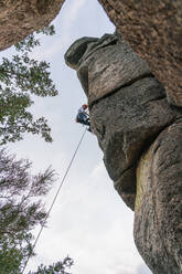 Männlicher Bergsteiger, der mit Sicherheitskarabiner und Seilen einen hohen Felsen erklimmt - ADSF40899