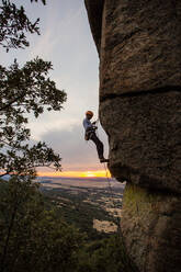 Männlicher Bergsteiger, der mit Sicherheitskarabiner und Seilen einen hohen Felsen erklimmt - ADSF40900