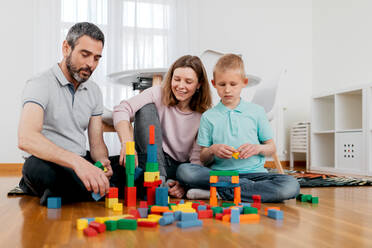 Cheerful parents with children playing with module blocks while playing in light house room - ADSF40931