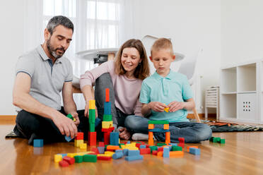 Fröhliche Eltern mit Kindern, die mit Bausteinen spielen, während sie in einem hellen Haus spielen - ADSF40931