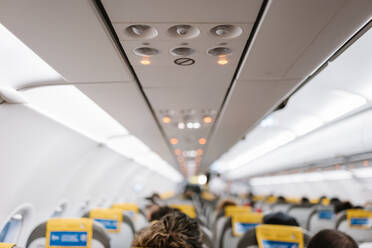 Unrecognizable passengers sitting on comfortable chairs under control panel inside contemporary aircraft during trip - ADSF40988