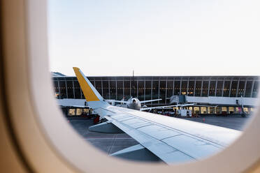 Wing of plane parked on aerodrome outside modern airport building behind window before departure - ADSF40989