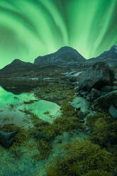 Herrlicher Blick auf die bunten Nordlichter, die den Nachthimmel über den felsigen Bergen in der Nähe des Sees im Winter auf den Lofoten erleuchten - ADSF41015