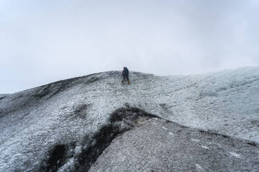 Von unten unerkennbarer Bergsteiger beim Klettern auf dem gefrorenen Felsen des Vatnajokull-Gletschers gegen einen bedeckten grauen Himmel an einem kalten Wintertag in Island - ADSF41037