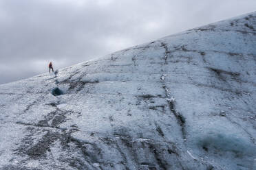 Abgeschnittene unerkennbare himmlische Eisformation des Vatnajokull-Gletschers mit Touristen vor einem wolkenverhangenen grauen Himmel an einem Wintertag in Island - ADSF41038