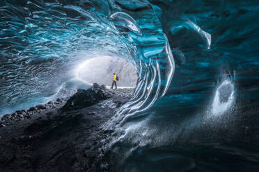 Tourist in Oberbekleidung, der bei der Erkundung einer Höhle im Vatnajokull-Gletscher an einem Wintertag in Island in der Nähe von unebenen Löchern in der Eisoberfläche steht - ADSF41053