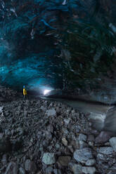 Tourist in Oberbekleidung, der bei der Erkundung einer Höhle im Vatnajokull-Gletscher an einem Wintertag in Island in der Nähe von unebenen Löchern in der Eisoberfläche steht - ADSF41054