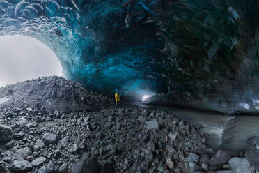 Tourist in Oberbekleidung, der bei der Erkundung einer Höhle im Vatnajokull-Gletscher an einem Wintertag in Island in der Nähe von unebenen Löchern in der Eisoberfläche steht - ADSF41055