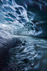 Rinnsale von sauberem Wasser, das von der blauen Decke einer Eishöhle auf den felsigen Boden des Vatnajokull-Gletschers fällt, an einem Frühlingstag in Island - ADSF41062