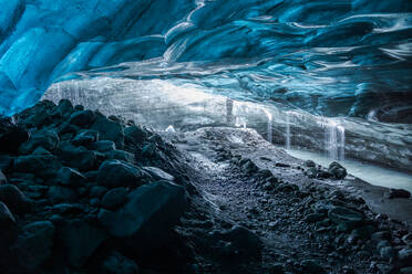 Rinnsale von sauberem Wasser, das von der blauen Decke einer Eishöhle auf den felsigen Boden des Vatnajokull-Gletschers fällt, an einem Frühlingstag in Island - ADSF41063