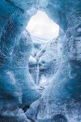 Von unten Eisspitzen, die das Loch in der Höhlendecke umgeben, gegen einen bedeckten grauen Himmel an einem Wintertag im Vatnajokull-Nationalpark in Island - ADSF41067